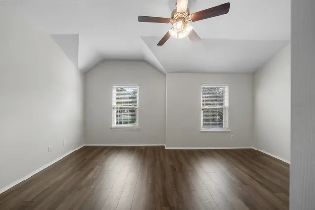 an empty room with wooden floor ceiling fan and windows