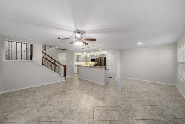 a view of an empty room with chandelier fan and kitchen view