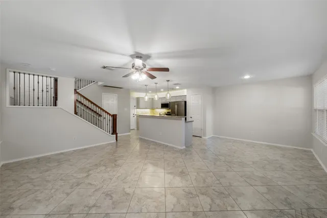 a view of an empty room with chandelier fan and kitchen view