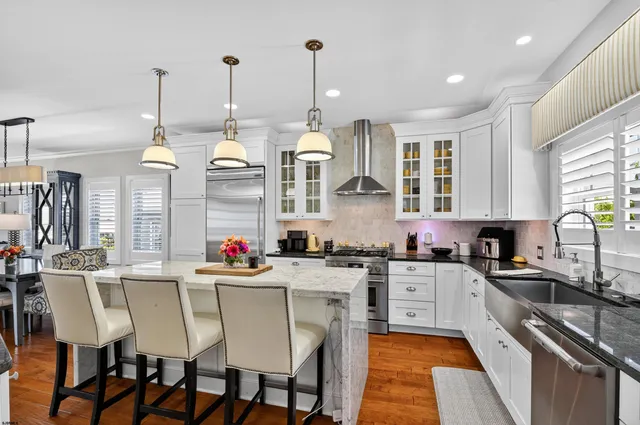 a kitchen with stainless steel appliances a stove a sink dishwasher a dining table chairs and couches with wooden floor