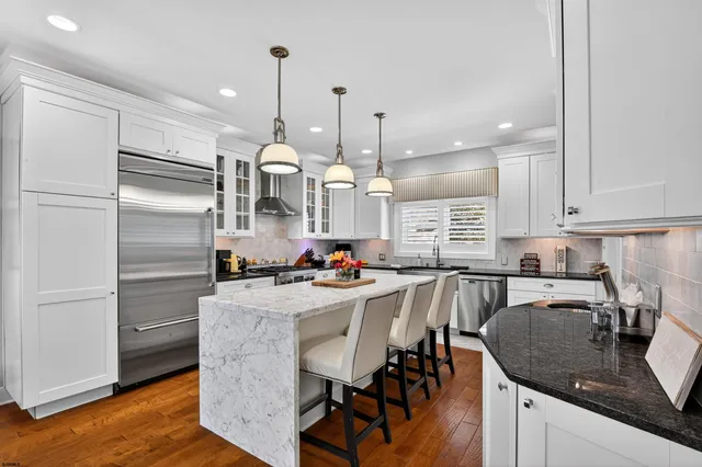a kitchen with stainless steel appliances granite countertop a kitchen island a stove a refrigerator a sink a dining table and chairs with wooden floor