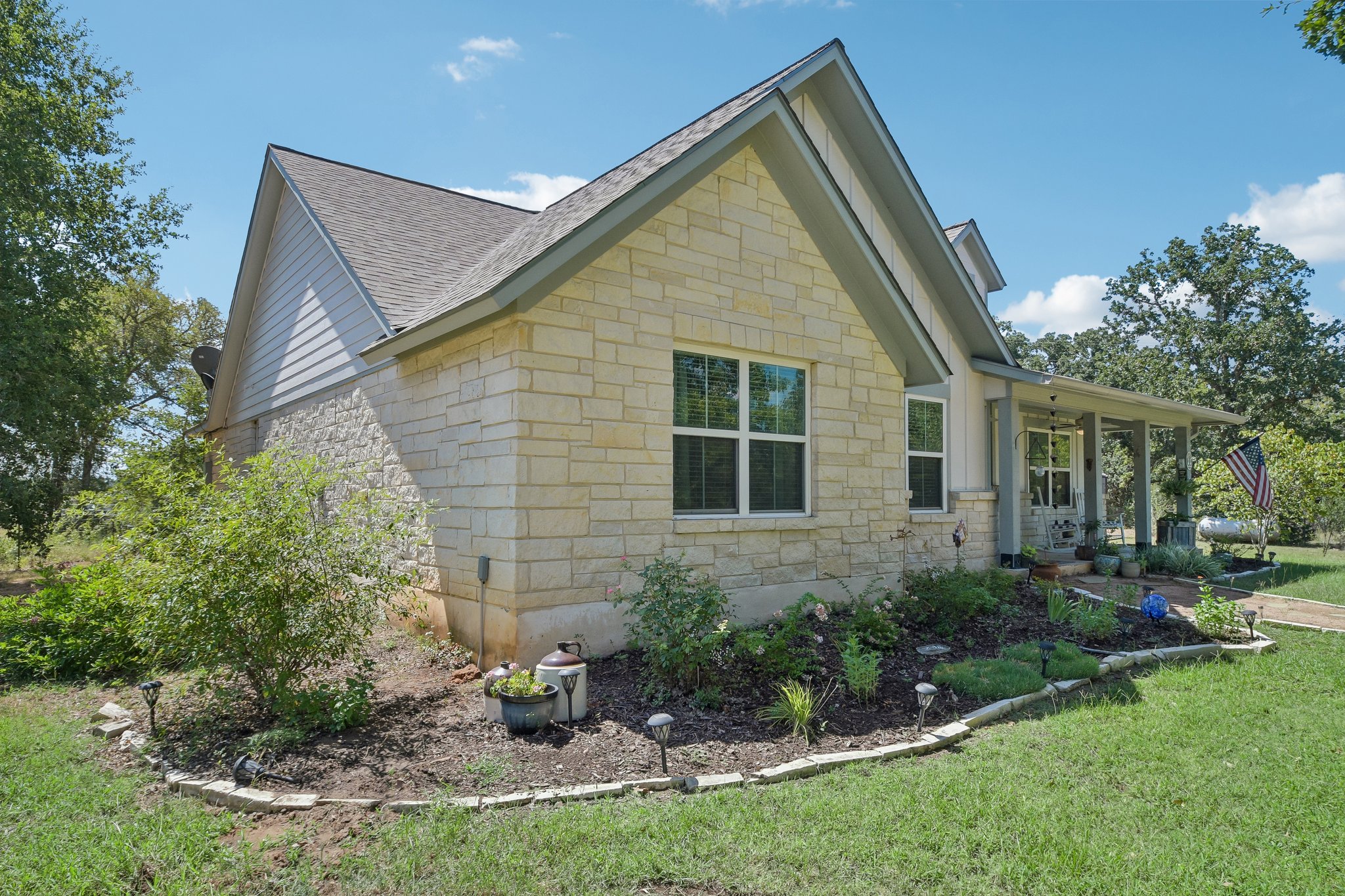596 Pleasant Grove Loop Elgin, TX 78621 - Photo 4 of 37 Stone and siding exterior walls harmonize with a gabled roofline above landscaped garden beds.