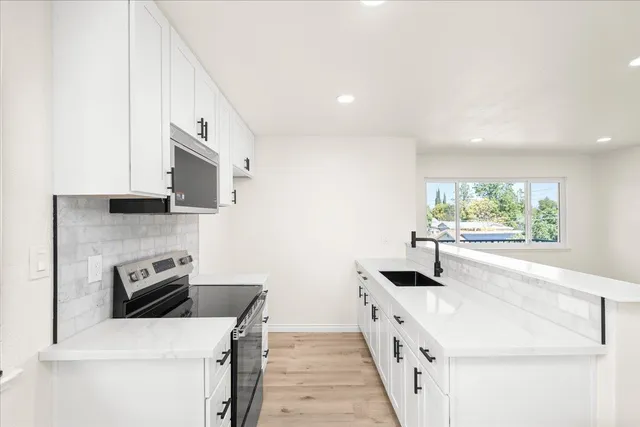 a kitchen with stainless steel appliances white cabinets a sink a stove a microwave a counter top and a refrigerator