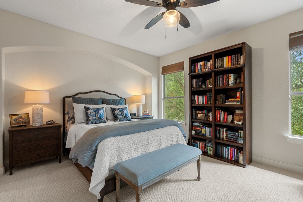 6708 Menchaca Road, Unit 2 Austin, TX 78745 - Photo 19 of 30 Carpeted bedroom featuring an arched wall niche, a ceiling fan with light fixture, two windows with wood-tone blinds, and a built-in bookshelf