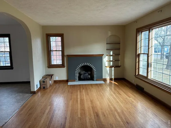 an empty room with windows a fireplace and wooden floor