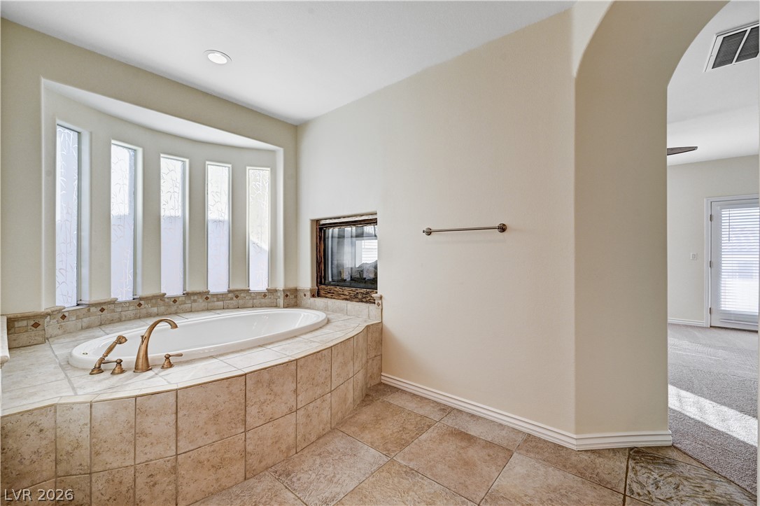 6761 Clay TABLET Street Las Vegas, NV 89149 - Photo 39 of 73 An arched opening reveals a relaxing bathroom featuring a tile-surround soaking tub and dual-sided fireplace.