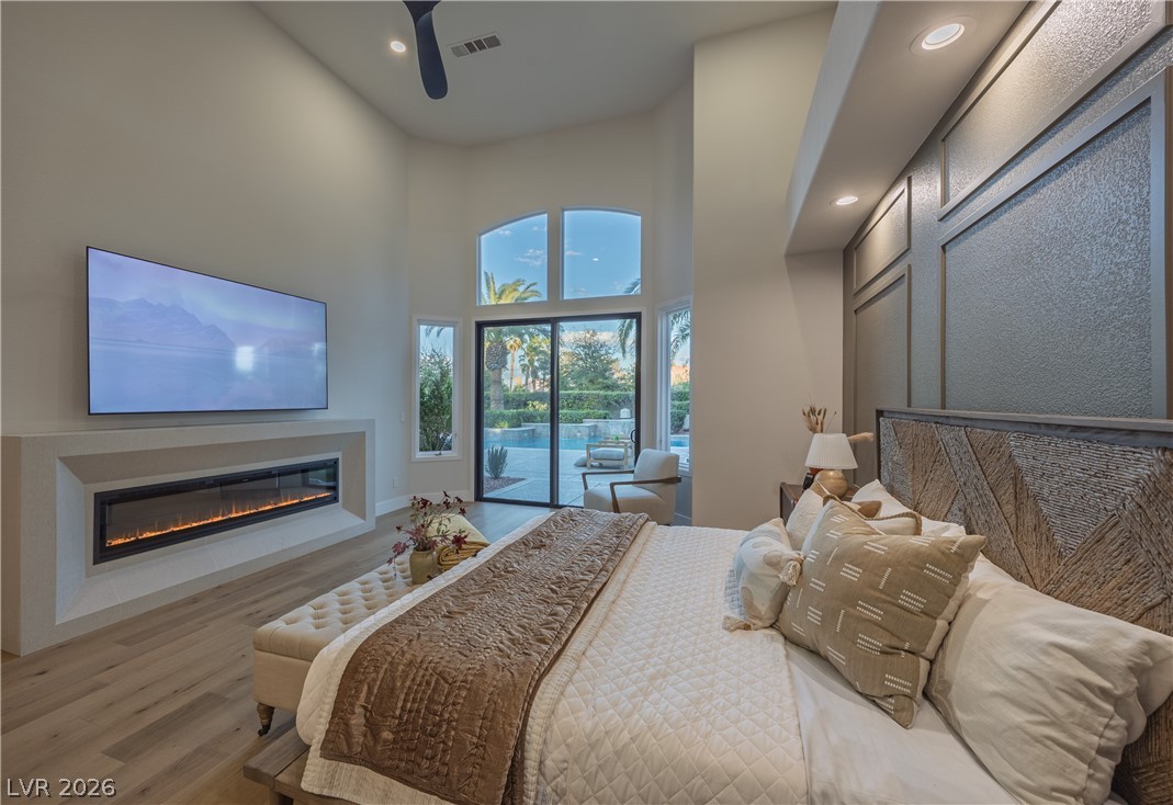 8800 Lusso Las Vegas, NV 89134 - Photo 42 of 85 Bedroom with access to exterior, light wood-type flooring, a glass covered fireplace, recessed lighting, and a high ceiling