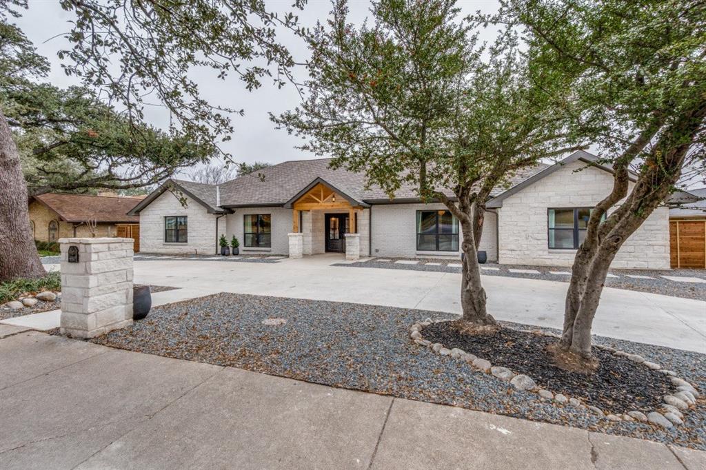 7115 Meadow Road Dallas, TX 75230 - Photo 22 of 22 The property features a light-colored brick exterior, a dark shingled roof, and a prominent front entrance with a wood-accented porch