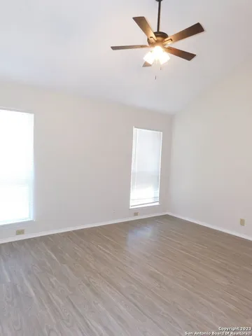 an empty room with wooden floor fan and windows