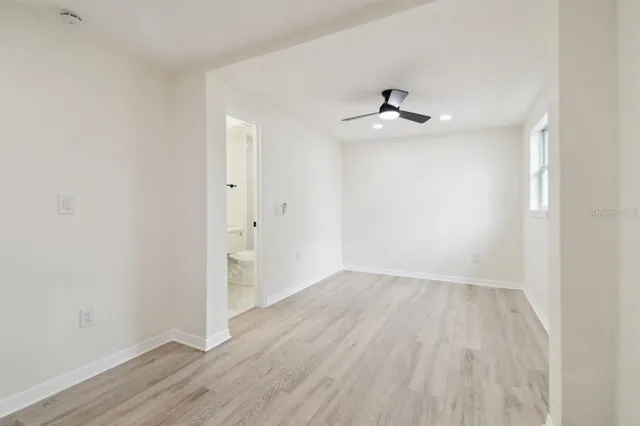 an empty room with wooden floor ceiling fan and window