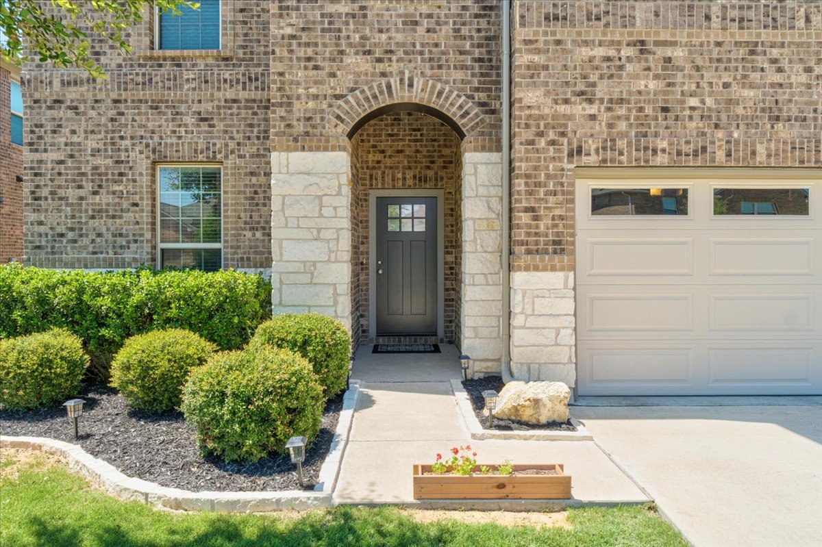 5408 Vanner Path Georgetown, TX 78626 - Photo 4 of 34 Brick and stone facade featuring an arched entryway, a paneled garage door with upper windows, a concrete walkway, and landscaped shrubbery with ground lighting