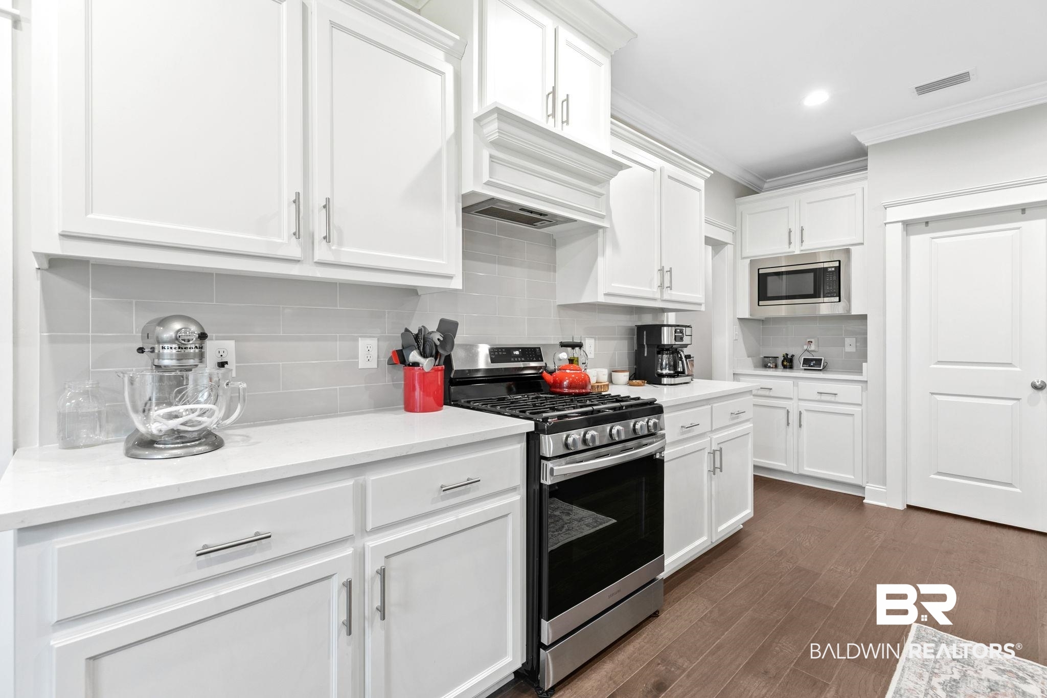 13233 Ibis Boulevard Daphne, AL 36527 - Photo 20 of 100 Contemporary kitchen featuring white cabinetry, light-toned countertops, a full suite of stainless steel appliances, a subway tile backsplash, and dark wood-finish flooring