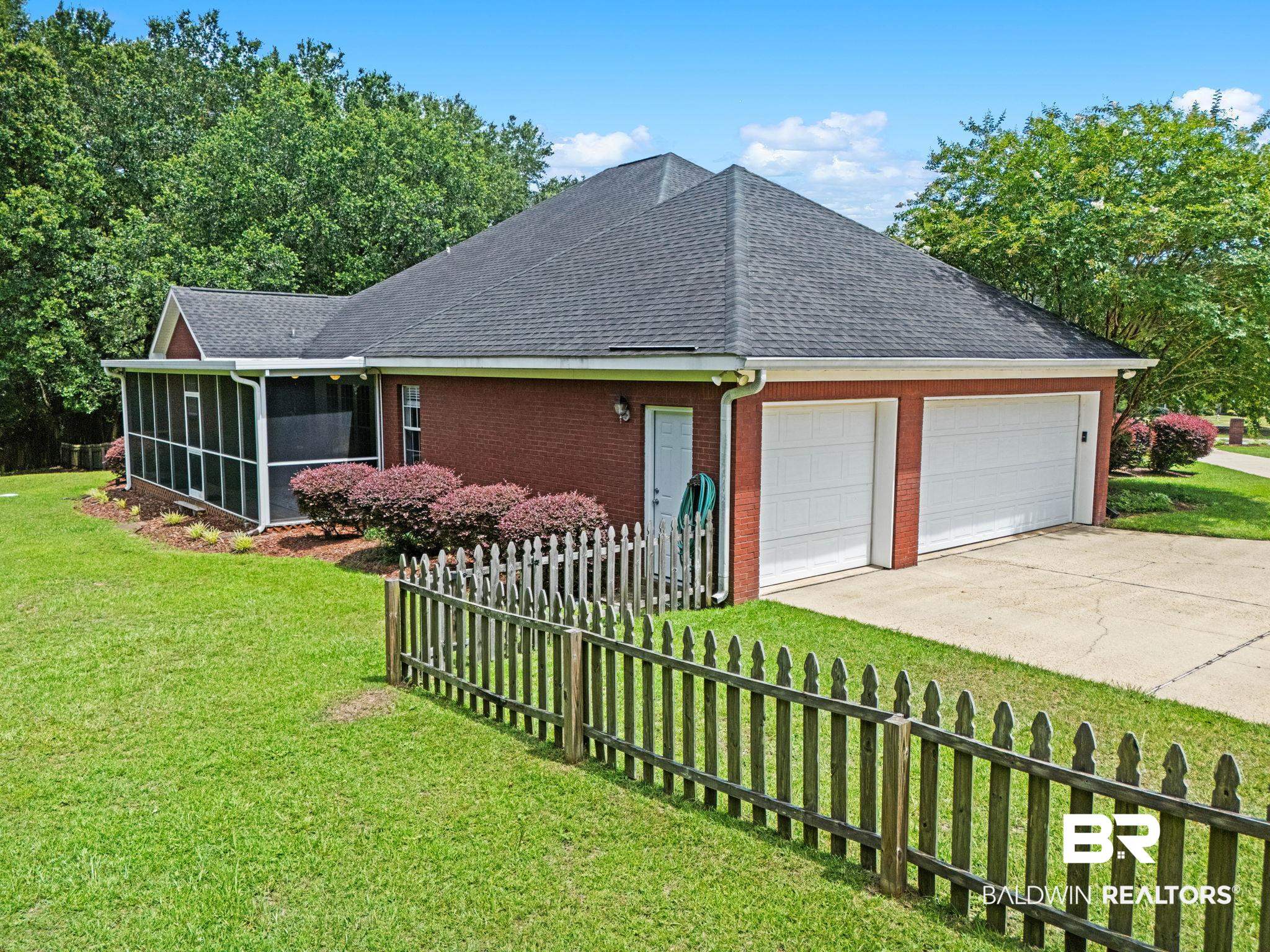 3176 Cedar Court Mobile, AL 36619 - Photo 31 of 33 Brick exterior featuring a screened porch, dual white garage doors, a concrete driveway, and a picket fence