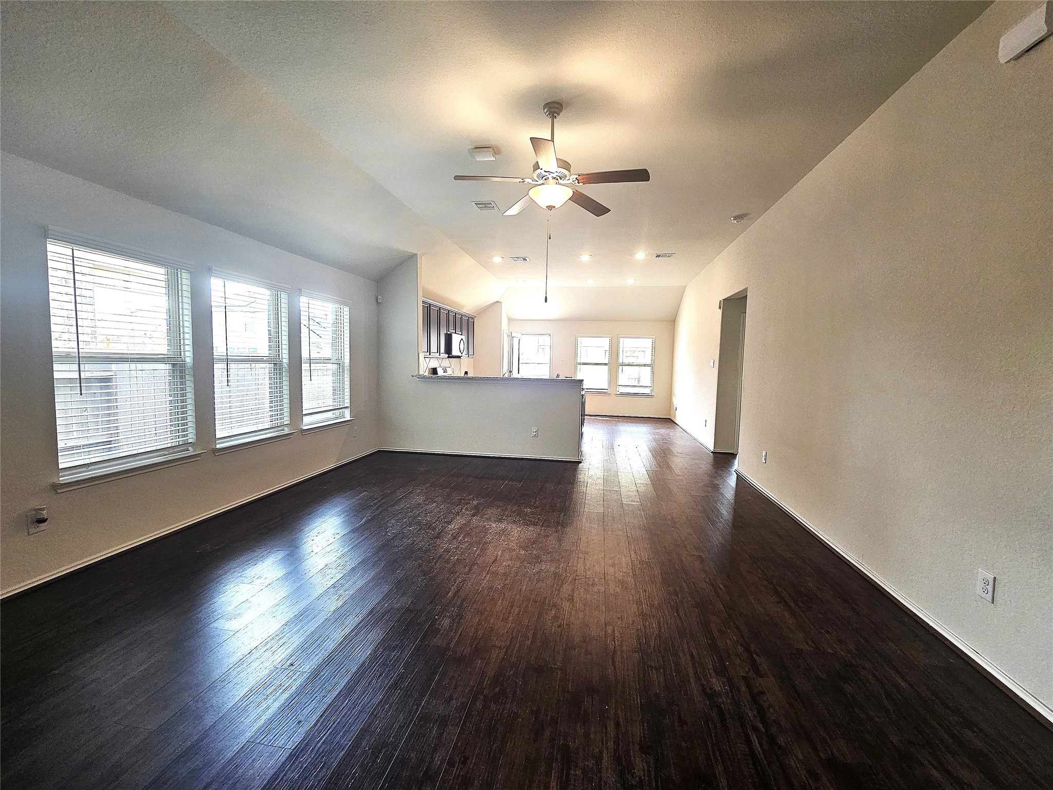 17439 Chester Valley Trail Hockley, TX 77447 - Photo 7 of 22 Spacious living area with dark hardwood floors, large windows providing natural light, and an open layout leading to the kitchen. Ceiling fan and neutral walls create a welcoming atmosphere.