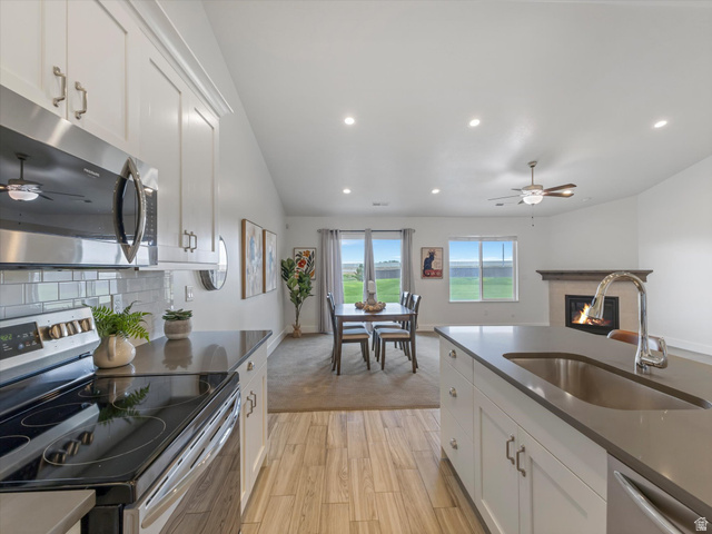 1278 South Grace Way Layton, UT 84041 - Photo 4 of 23 Open-concept living area featuring a kitchen island with an undermount sink, stainless steel appliances, white cabinetry, a subway tile backsplash, and a fireplace in the background