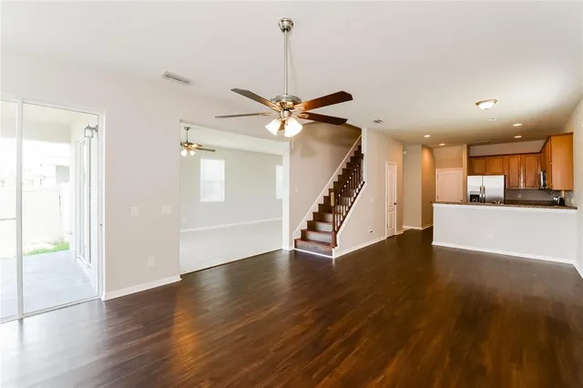 a view of an empty room with wooden floor and a ceiling fan