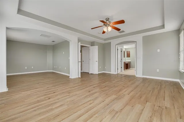a view of an empty room with wooden floor and a ceiling fan