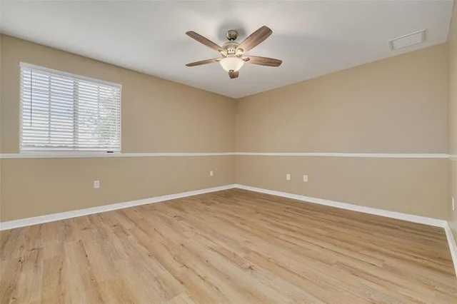 an empty room with wooden floor fan and windows
