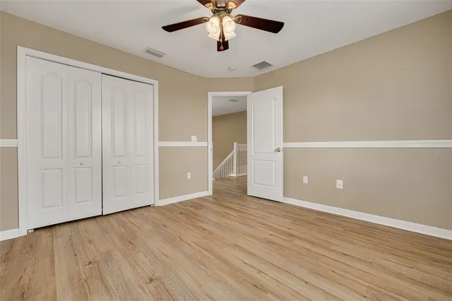 an empty room with wooden floor chandelier fan and windows