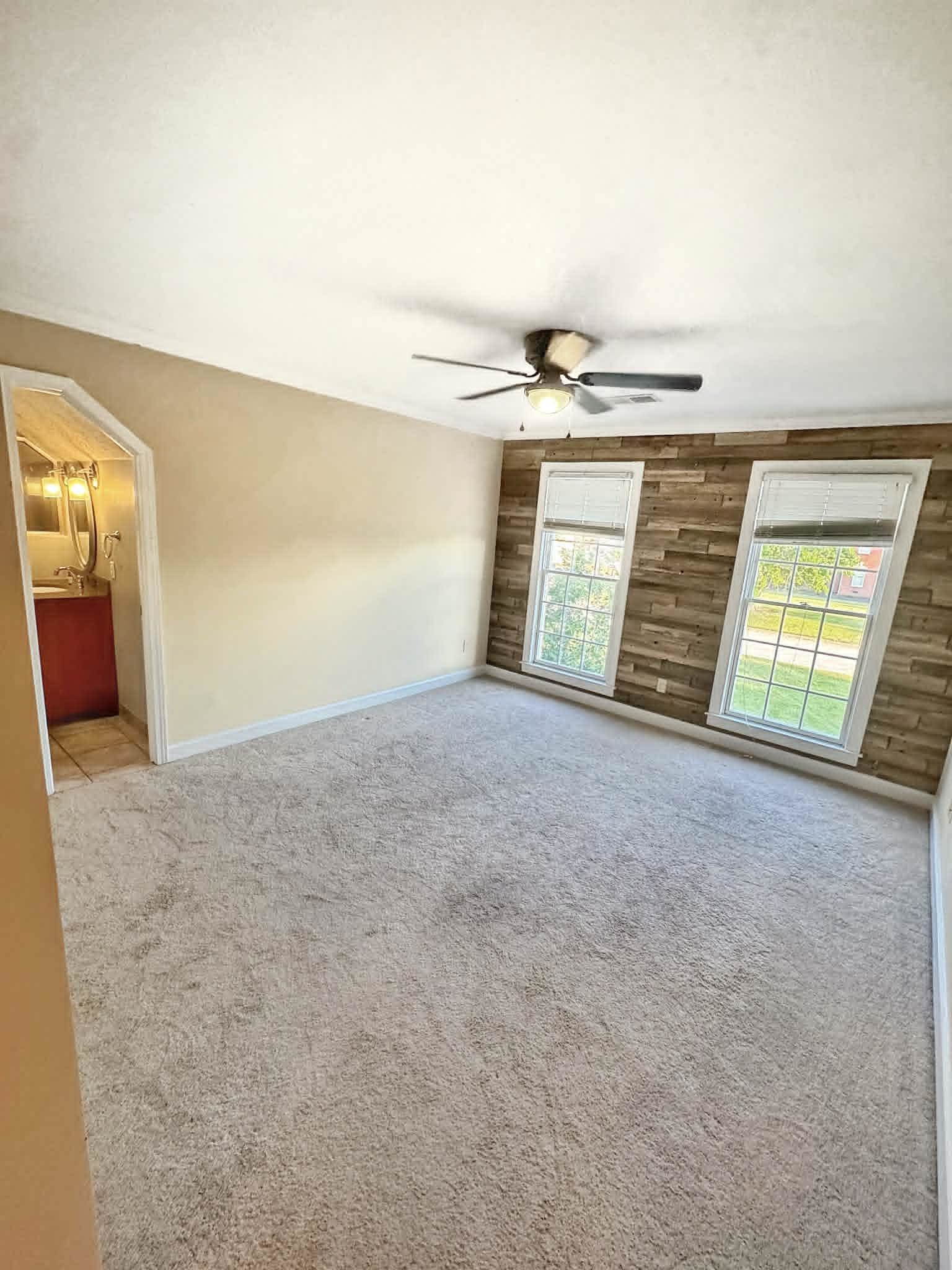 37 Crownpointe Cove Jackson, TN 38305 - Photo 26 of 39 Spacious room featuring neutral carpet flooring, a decorative wood-panel accent wall, and two large windows providing natural light