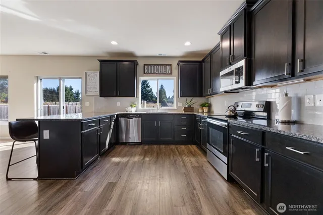 a kitchen with stainless steel appliances granite countertop wooden cabinets a refrigerator a sink a stove a microwave and wooden floors