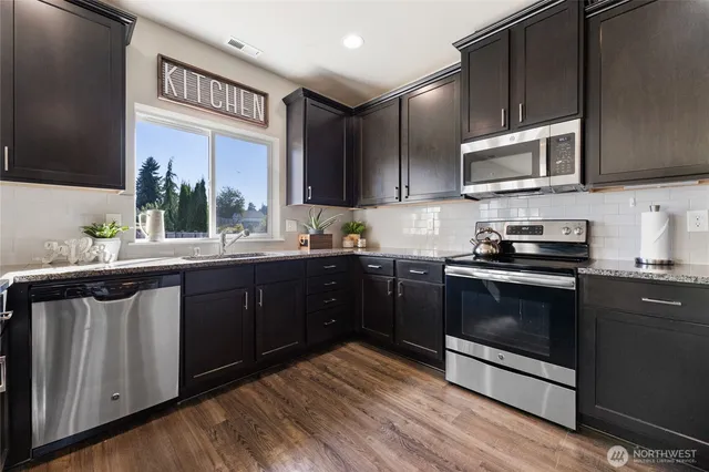 a kitchen with stainless steel appliances granite countertop a stove a sink dishwasher and a microwave oven on the wooden floor