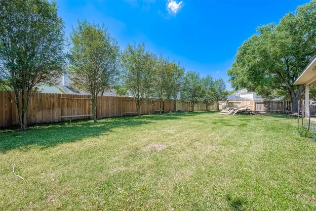 a view of a backyard with large trees and wooden fence