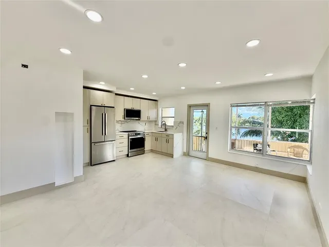 a large white kitchen with stainless steel appliances granite countertop a large window and a kitchen view