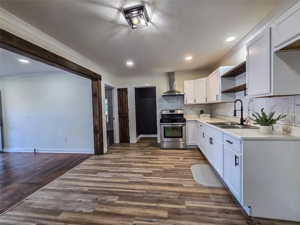 a large kitchen with kitchen island a stove a sink dishwasher a refrigerator and white cabinets with wooden floor