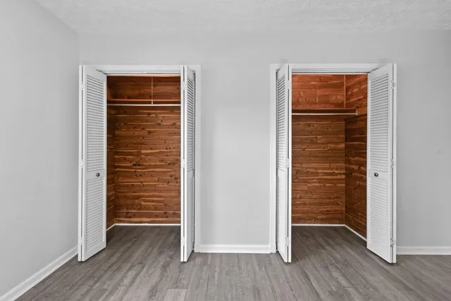 an empty room with wooden floor closet and windows