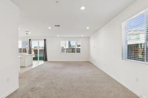 a view of an empty room with kitchen and window