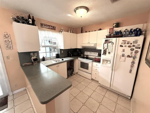 a kitchen with granite countertop a refrigerator a sink a stove and white cabinets