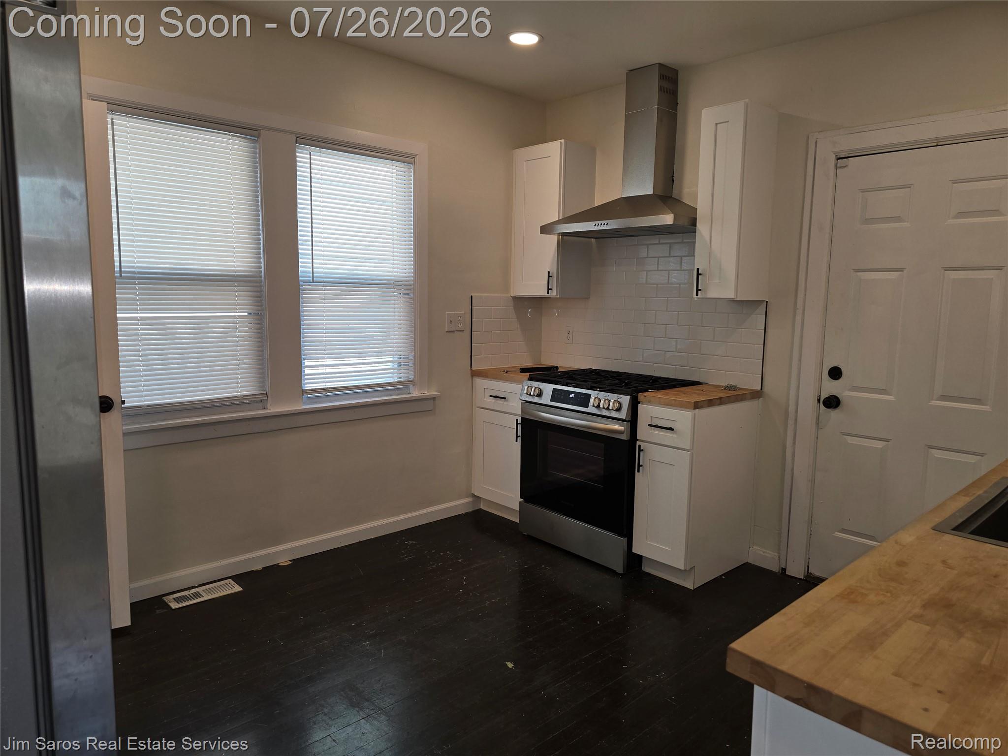 1629 Alter Road Detroit, MI 48215 - Photo 6 of 12 Kitchen featuring dark wood-finish flooring, white shaker cabinetry, stainless steel range with matching hood, subway tile backsplash, and light wood countertops