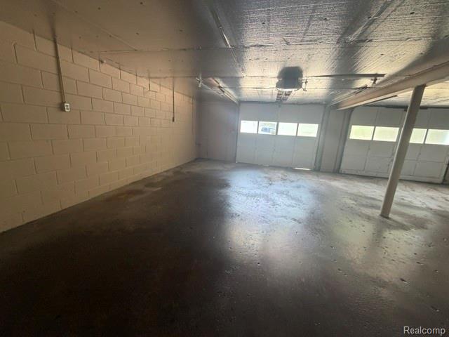 1404 South Graham Road Flint, MI 48532 - Photo 16 of 17 Spacious garage featuring two overhead doors with frosted window inserts, painted concrete block walls, and a finished concrete floor