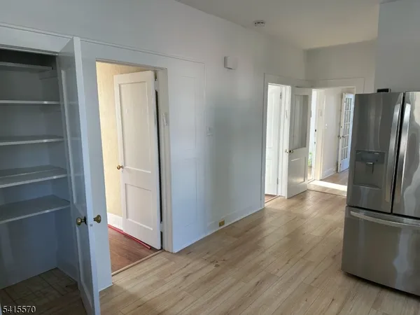 a view of a refrigerator in kitchen and an empty room with wooden floor windows