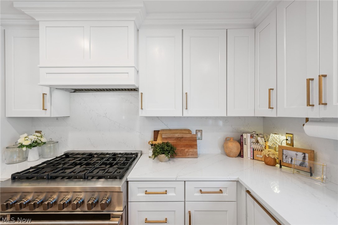 25870 Kennedy Ridge Road North Olmsted, OH 44070 - Photo 18 of 50 Stainless steel gas range with a custom range hood, white shaker cabinetry, white countertops, and a full-height stone backsplash