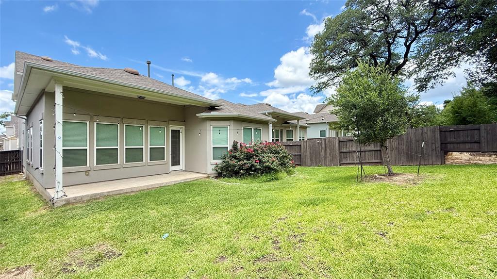 601 C-Bar Ranch Trail, Unit 27 Cedar Park, TX 78613 - Photo 29 of 29 Expansive grassy yard featuring a covered concrete patio, multiple large windows, mature perimeter trees, and a privacy fence
