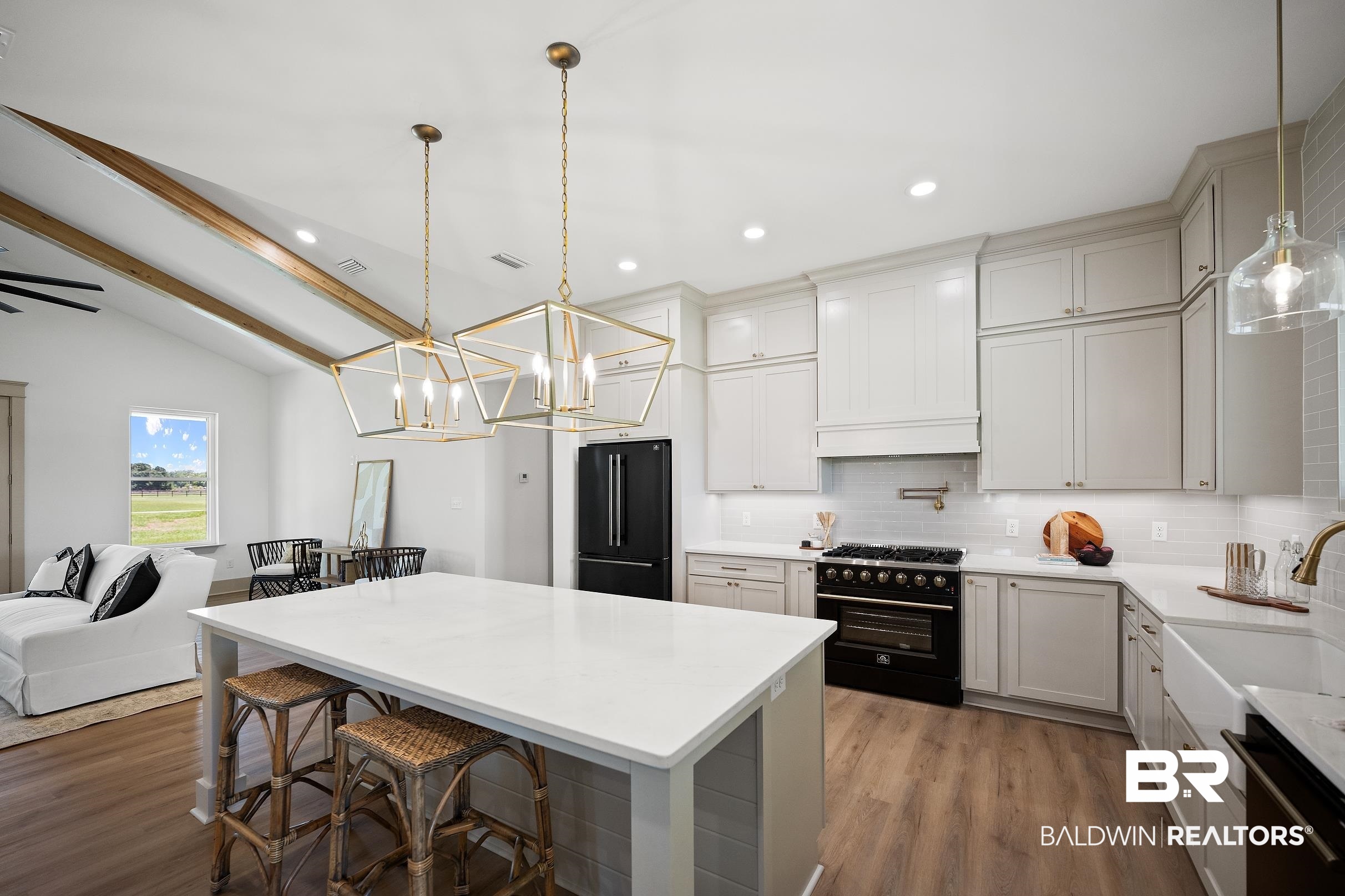 13111 Gopher Court Elberta, AL 36530 - Photo 9 of 41 Open-concept kitchen featuring light wood-finish flooring, a white island with a solid surface countertop, white shaker cabinetry, a black range, and a white farmhouse sink