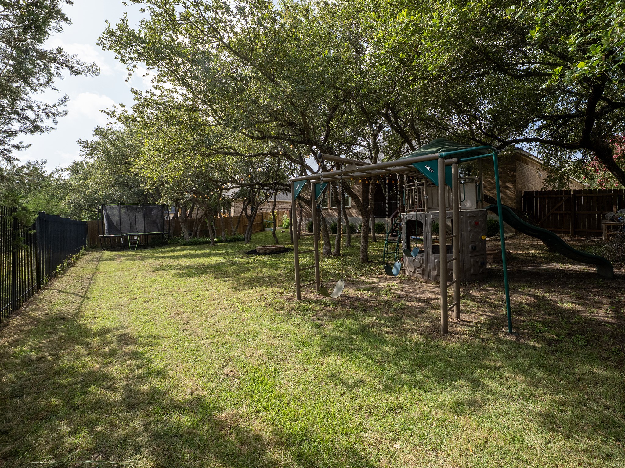 572 Big Meadow Road Austin, TX 78737 - Photo 26 of 32 An inviting private yard featuring a swing set, slide, and trampoline beneath mature shade trees.