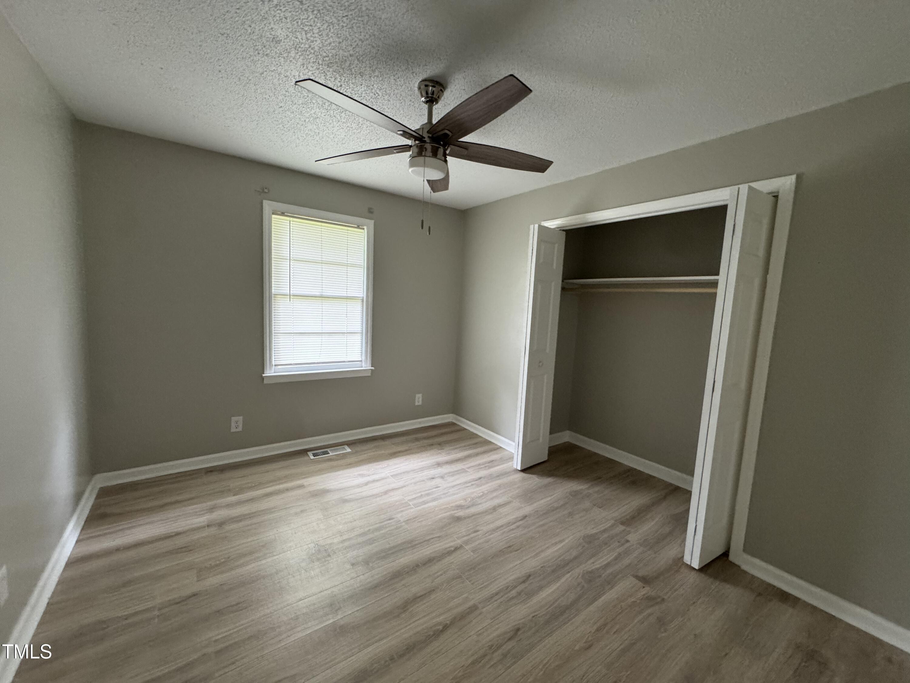 1064 Abbott Road Henderson, NC 27537 - Photo 7 of 9 an empty room with wooden floor fan and windows