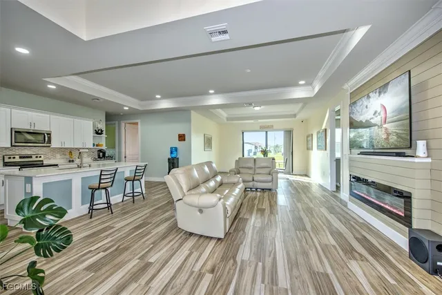 a living room with stainless steel appliances furniture wooden floor and a kitchen view