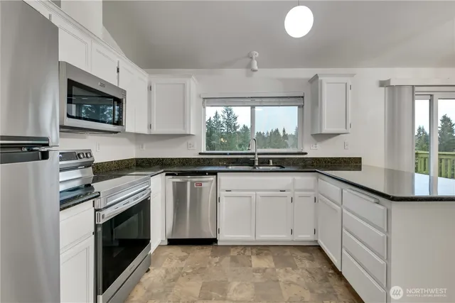 a kitchen with granite countertop white cabinets stainless steel appliances a sink and a window