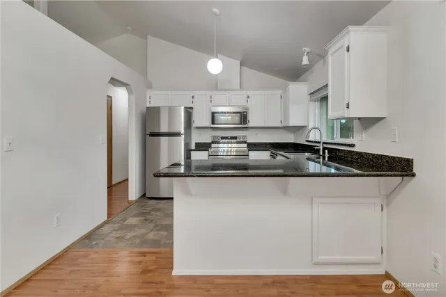 a kitchen with stainless steel appliances granite countertop a sink a stove a refrigerator and white cabinets