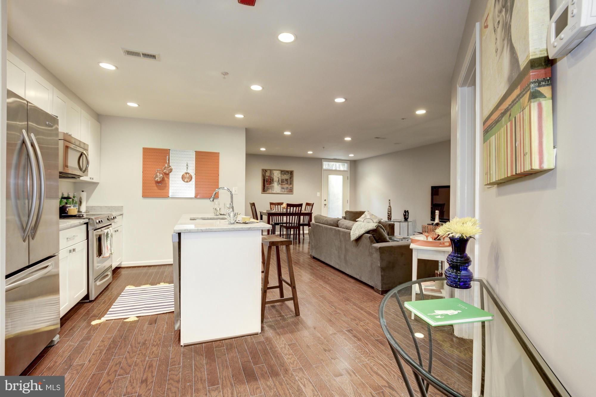 a living room with stainless steel appliances furniture wooden floor and a kitchen view