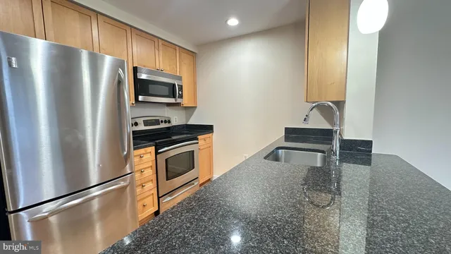 a kitchen with stainless steel appliances granite countertop a refrigerator a stove and a sink with wooden floor