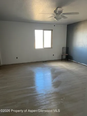 an empty room with wooden floor fan and windows
