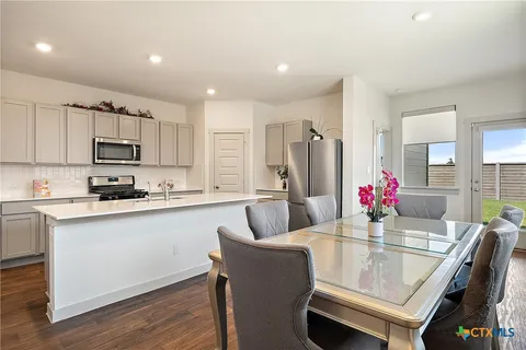 a kitchen with kitchen island granite countertop a dining table chairs refrigerator and microwave