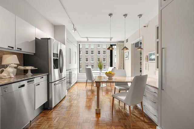 a kitchen with stainless steel appliances kitchen island granite countertop a refrigerator a stove and white cabinets with wooden floors