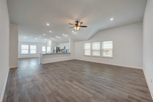 an empty room with wooden floor ceiling fan and windows