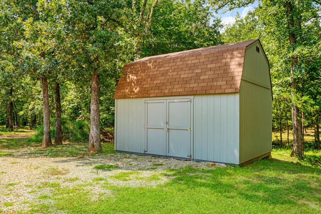 821 County Road Paris, TX 75462 - Photo 38 of 40 Gable roof storage shed featuring two front entry doors, vertical panel siding, and a surrounding lawn with mature trees
